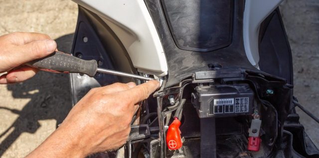Motocycliste installant une batterie neuve sur sa moto dans un garage.