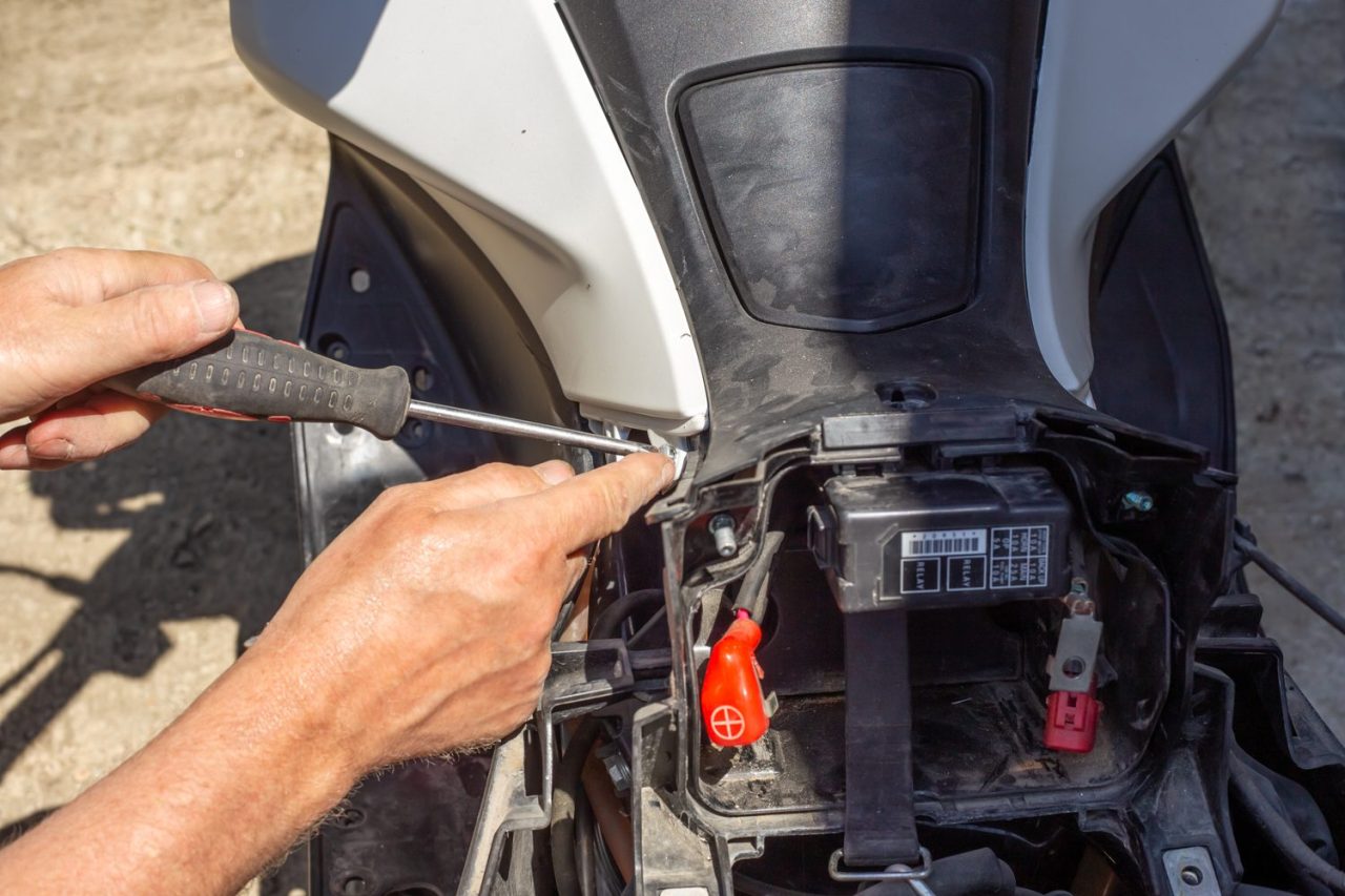 Motocycliste installant une batterie neuve sur sa moto dans un garage.