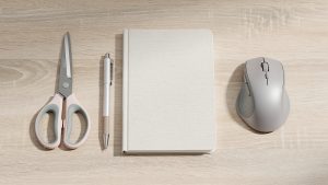 Bureau lumineux vu de dessus avec des ciseaux pour gaucher, un stylo à séchage rapide, un cahier vierge et une souris ergonomique pour la main gauche.