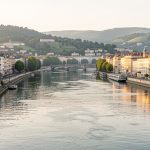 Vue urbaine réaliste de Lyon depuis les quais de la Saône, avec les immeubles anciens, la Presqu’île et les collines baignés par une douce lumière de fin de journée.